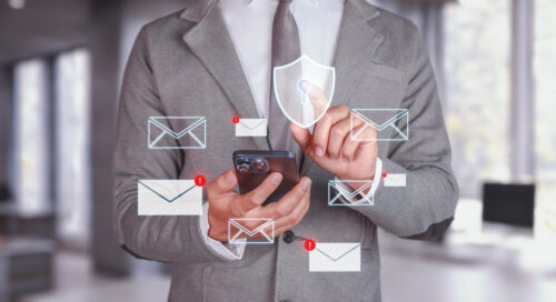 Man in gray suit holds his phone while white email security icons rotate around phone