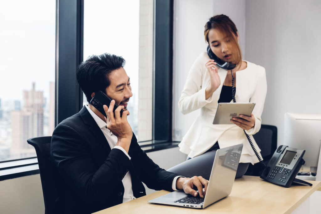 Two business people use a VoIP phone system to place phone calls