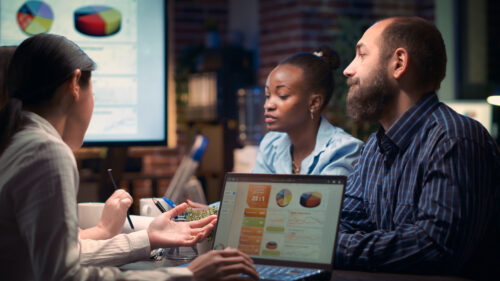 A group of young people sit around a table discussing revenue figures